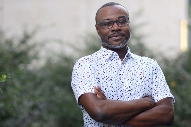 a black man in a white button down shirt with his arms crossed